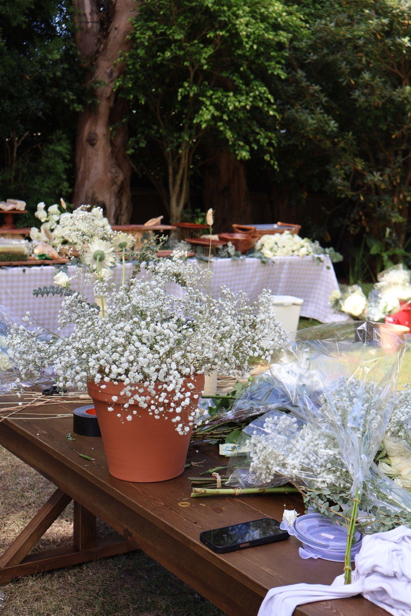 Baby’s breath in a terracotta pot and bundles of white flowers on a wooden table while the buffet is set up behind