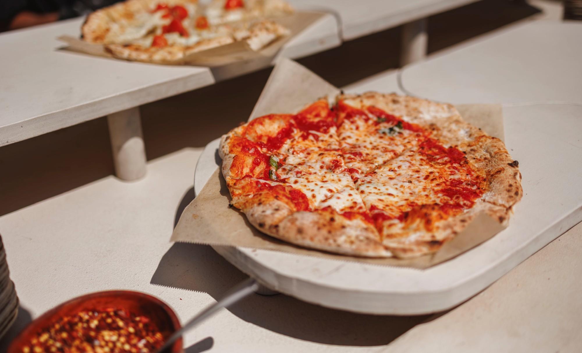 A wood-fired margherita pizza on a white serving board