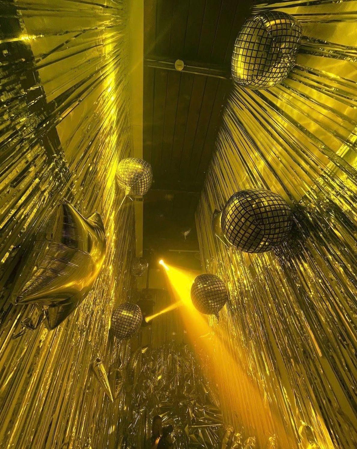 A corridor of gold fringe curtains with mirrored disco ball balloons and a single yellow spotlight